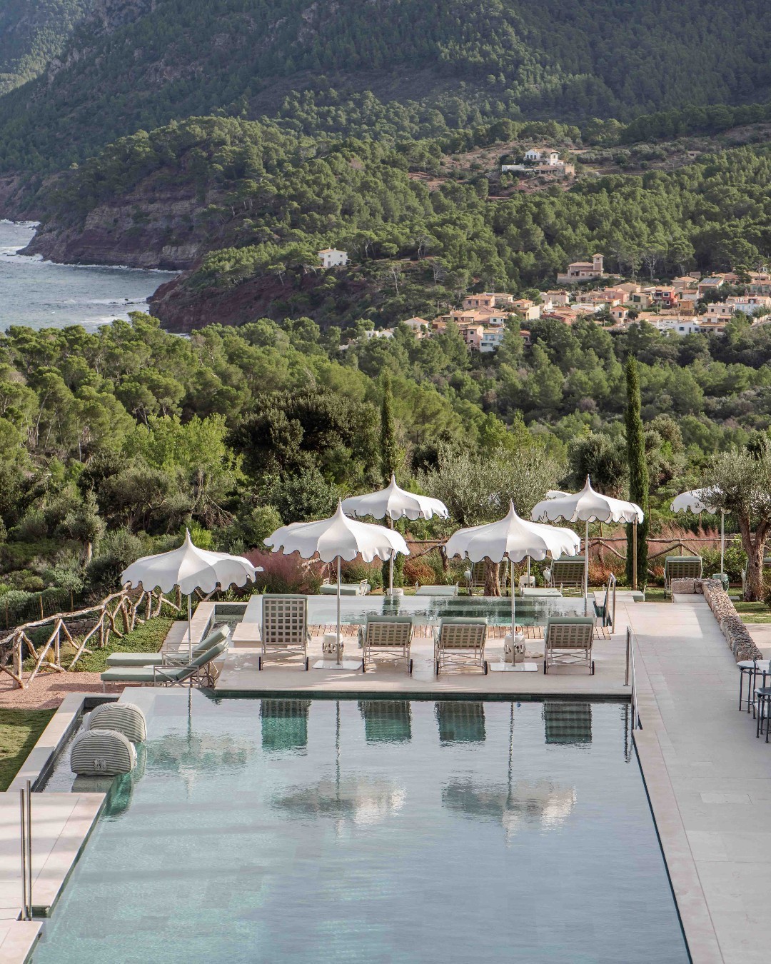 Infinity pool at Son Bunyola with white umbrellas, sea view, and lush Tramuntana mountains in Mallorca, Spain.