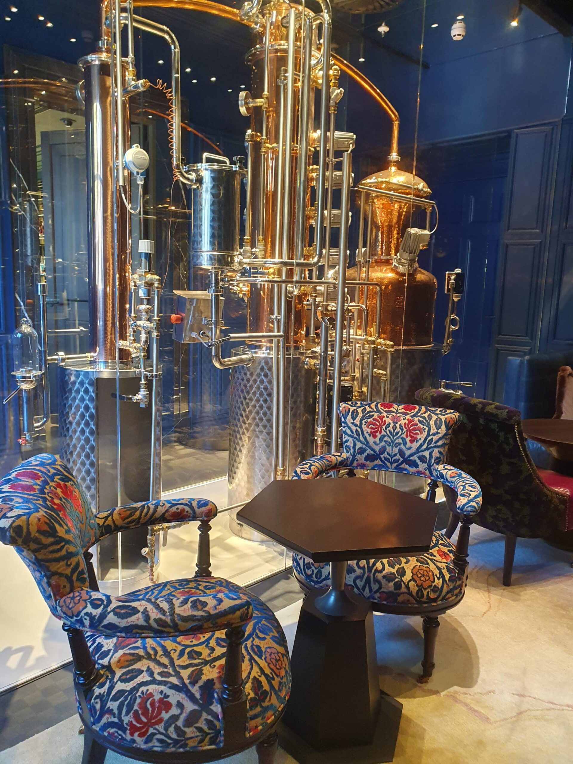 Stylish distillery space at Rosewood Amsterdam featuring copper distillation pipes, blue walls, and cozy seating for cocktails or drinks