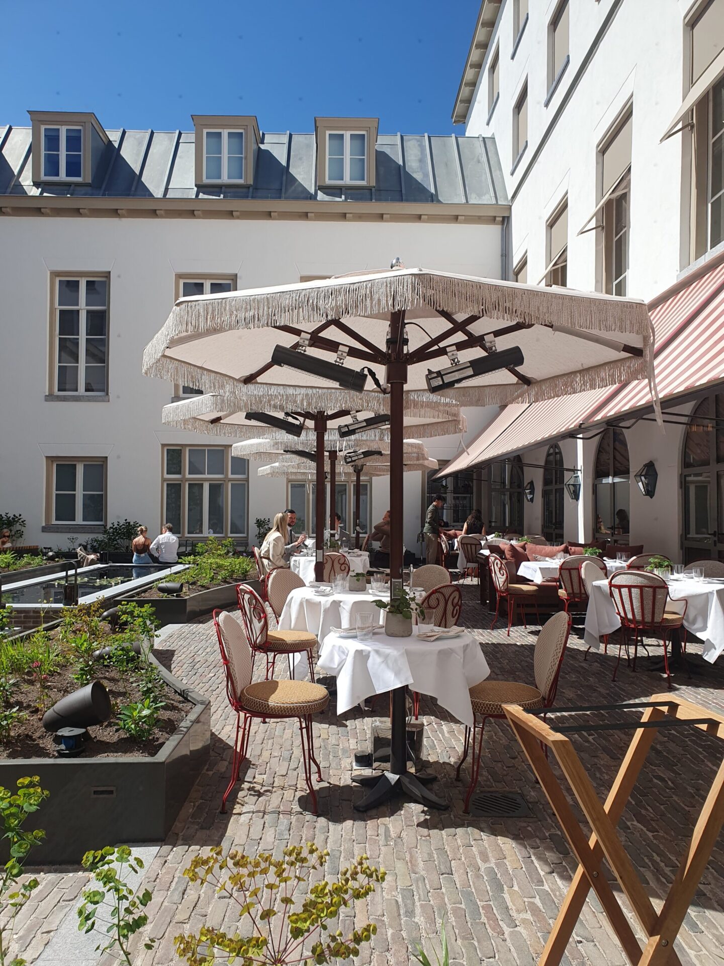Tranquil courtyard terrace with parasols at Eeuwen restaurant, Rosewood Amsterdam