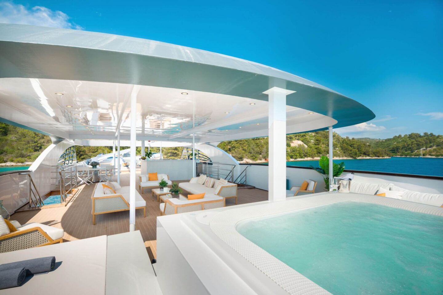 Luxury yacht deck with jacuzzi and lounge seating overlooking the Croatian coastline, styled with soft furnishings and surrounded by calm blue water.